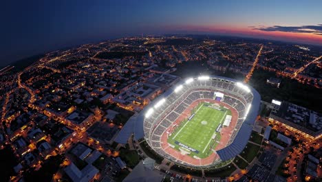 nighttime aerial view revealing illuminated stadium nestled within vibrant urban cityscape, showcasing dynamic architectural contrast during twilight hours