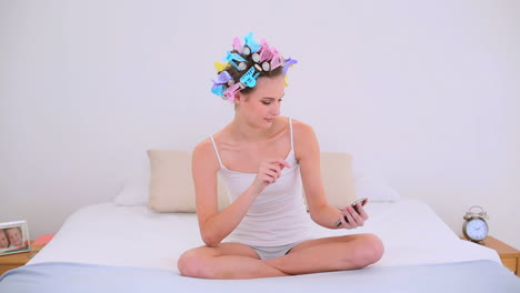 Young-model-in-hair-rollers-sending-a-text-on-her-bed