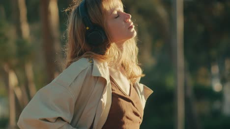 Woman-listening-to-music-with-headphones-basks-in-sun-with-eyes-closed-outdoors