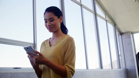 Executive-standing-near-window-and-using-mobile-phone