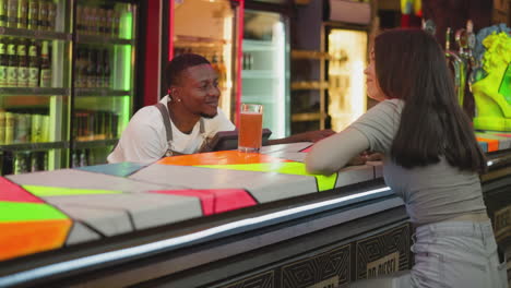 barman tells funny story to sad woman at counter. interested lady listens to barkeeper jokes ordering beer in night club. barkeeper treats girlfriend