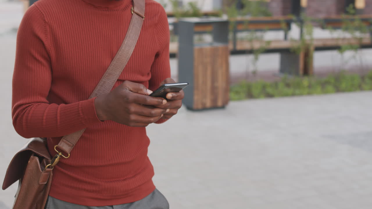 Uomo d'affari afroamericano che usa lo smartphone mentre cammina in centro