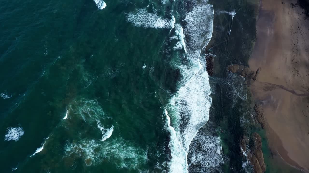 Scenic aerial bird's eye view of ocean white waves and beach on the California coastal shore.