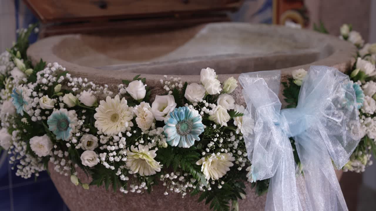 stone baptismal font adorned with white flowers and baby blue bow