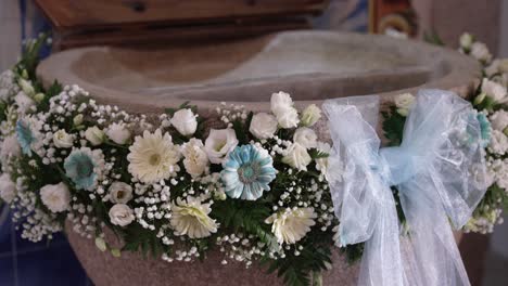 stone baptismal font adorned with white flowers and baby blue bow