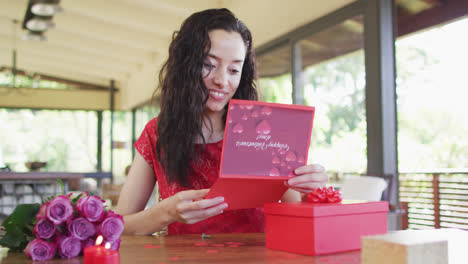 happy biracial woman opening valentines card and presents at home