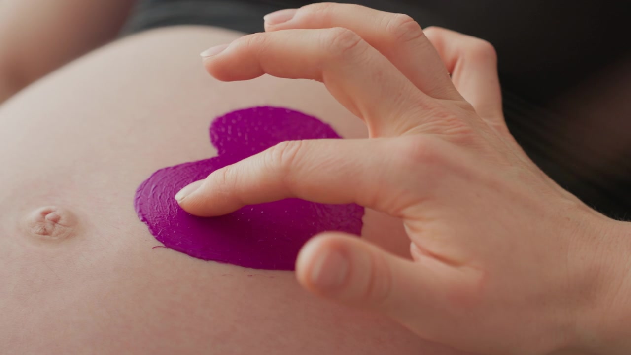 Pancia incinta con un cuore viola che viene toccata delicatamente