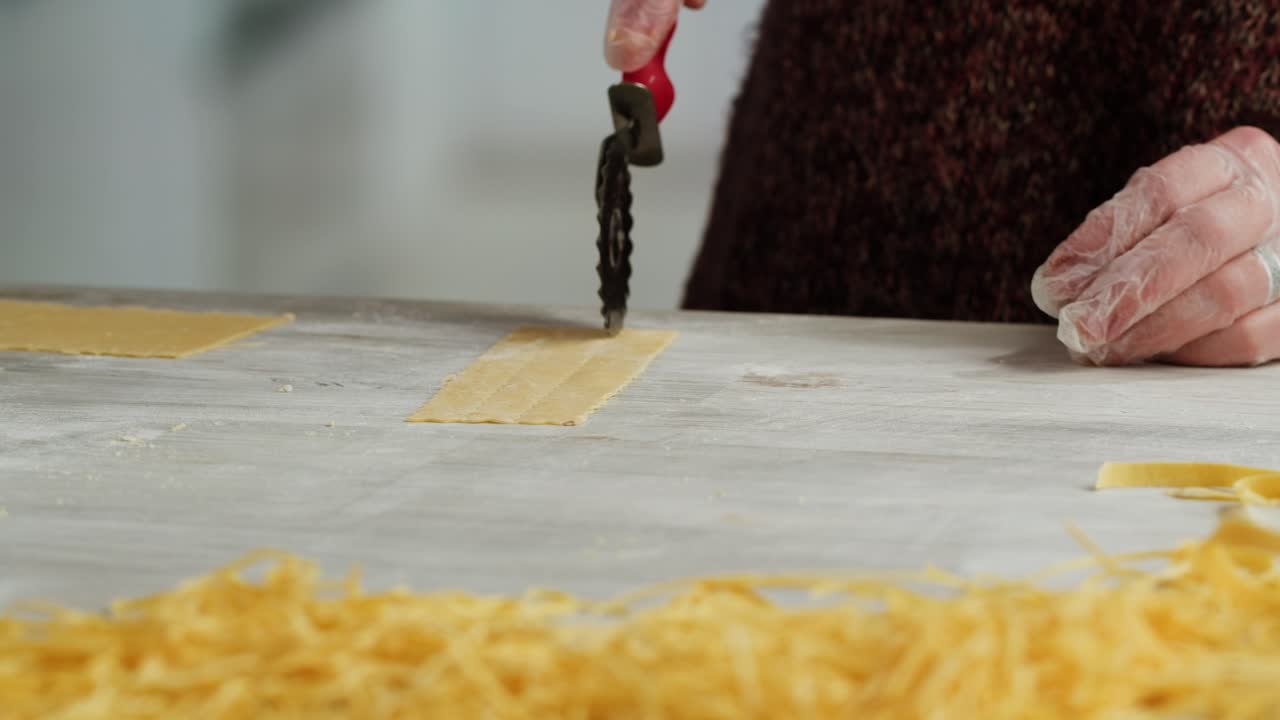 Close-up of Hands Cutting Fresh Pasta Dough with a Roller