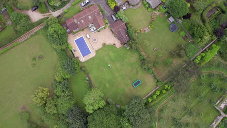 Rotating-Aerial-Shot-of-Man-Mowing-Lawn-of-Home-on-Summer’s-Day-using-Ride-On-Lawnmower-from-Birds-Eye-View-Perspective