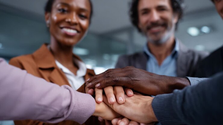 In a collaborative environment, diverse individuals unite their efforts by placing their hands together in a symbol of teamwork, cooperation, and shared commitment, showcasing unity and harmony in the workplace