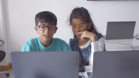 Couple of serious classmates in glasses collaborating on project