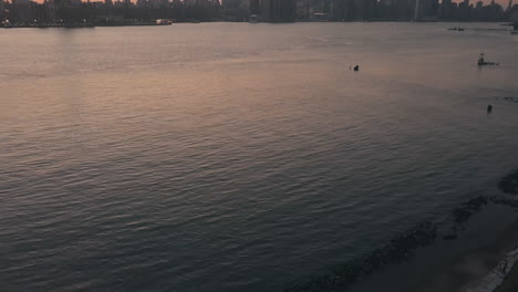 AERIAL:-Slow-Tilt-up-over-East-River-Waves-showing-Manhattan-New-York-City-Skyline-in-Beautiful-Dawn-Sunset-Orange-Light