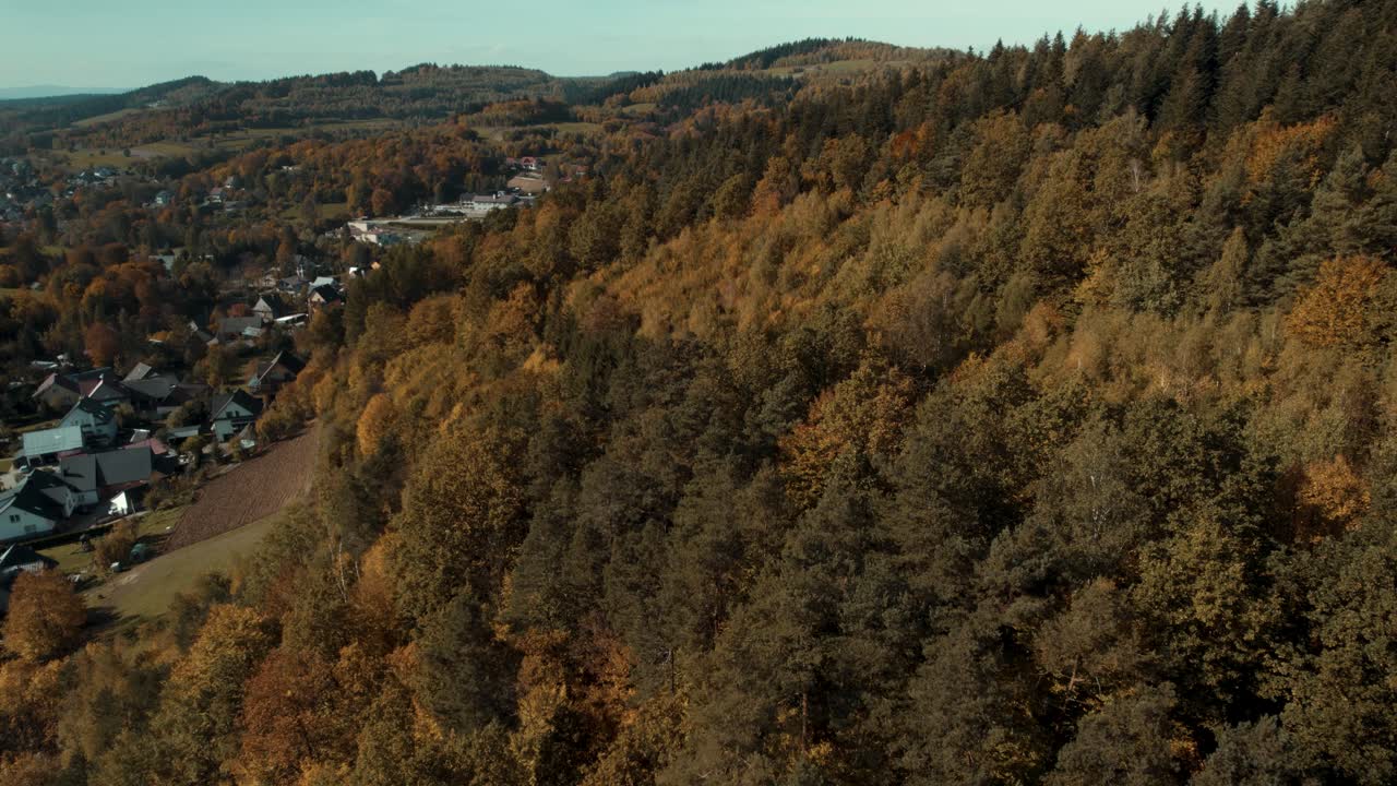 vista de pájaro del colorido bosque otoñal a la luz del día con el pueblo y las montañas al fondo