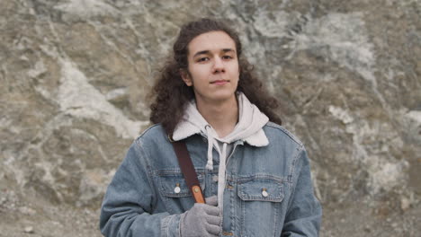 front view of a teenage boy with long hair and winter clothes smiling and looking at camera on the mountain on a windy day