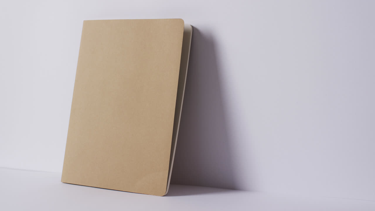 Close up of closed beige book leaning on wall with copy space on white background in slow motion