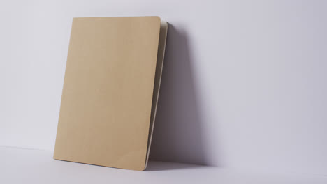 close up of closed beige book leaning on wall with copy space on white background in slow motion