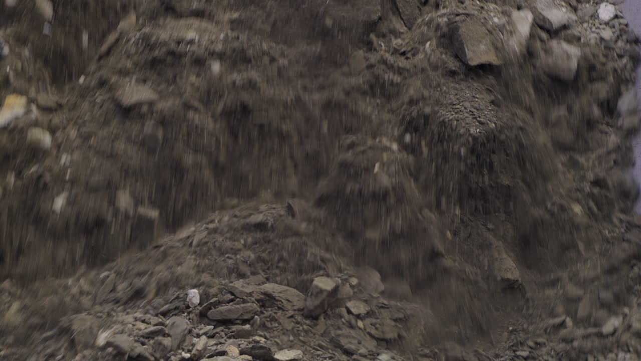 Primo piano di materiale minerale roccioso che viene rovesciato dalla benna di un dumper da miniera in attesa di lavorazione.