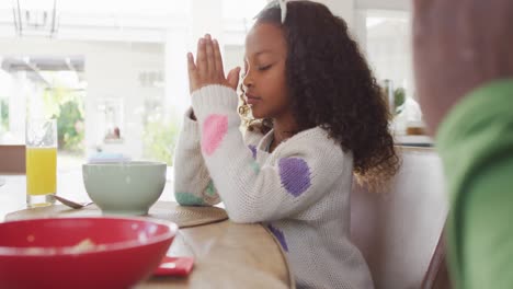 Video-of-african-american-daughter-and-father-saying-grace-at-table-before-family-meal