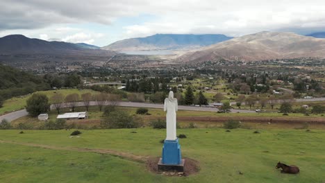 'El-Cristo'-of-Tafí-del-Valle-viewed-from-behind-by-a-drone,-with-the-beautiful-valley-and-La-Angostura-Dam-in-the-background