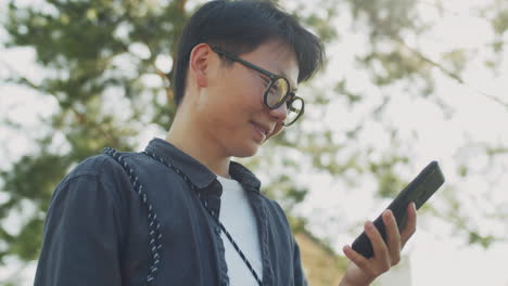 Joven-Asiática-De-Pie-Al-Aire-Libre-Y-Usando-Un-Teléfono-Inteligente