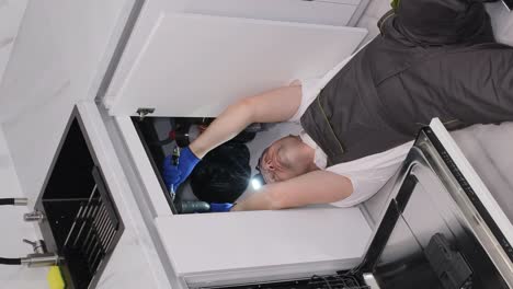 young plumber in uniform repairing sink in kitchen room a call to the home of a master plumber