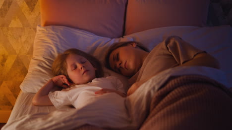 pretty little girl and mommy sleep in wide bed at night