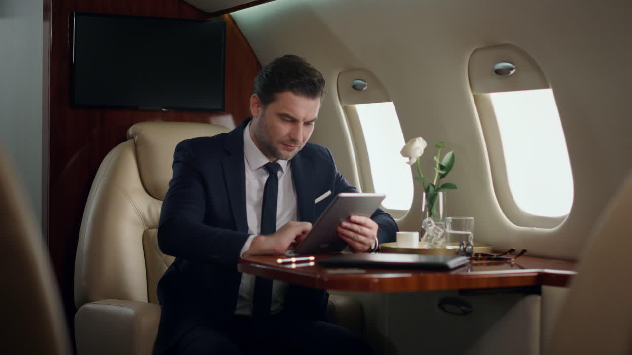 Uomo d'affari stressato che lavora al tablet in aereo. Schermo touch pad professionale
