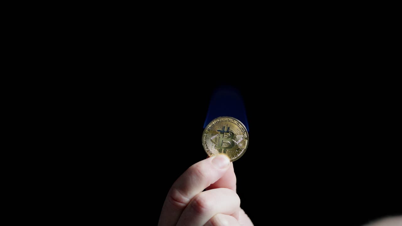 Person holding one bitcoin uses lighter to set it on fire, blue flame burning on black background.