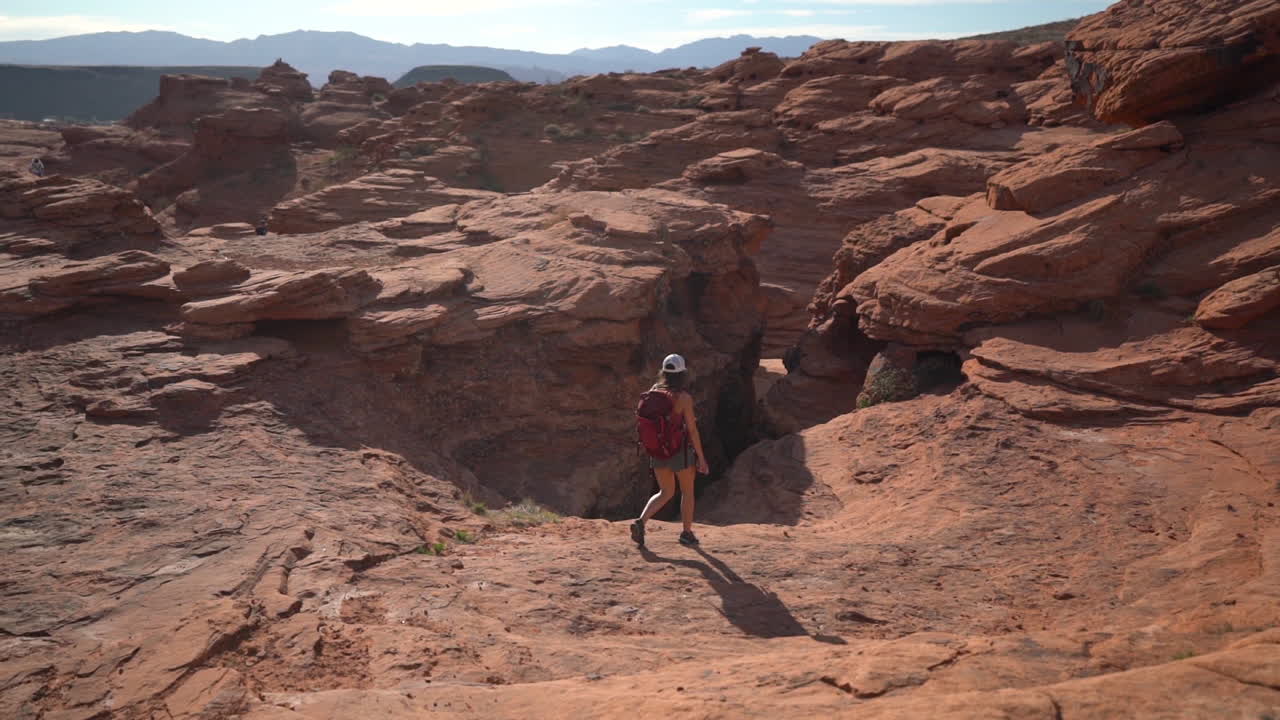 vista de atrás de una excursionista solitaria caminando sobre rocas rojas en el paisaje del desierto en un día caluroso y soleado