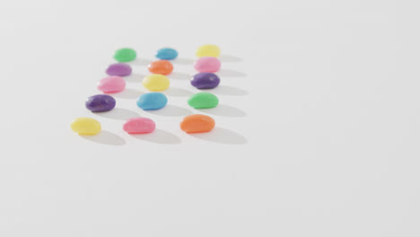 video of overhead view of rows of multi coloured sweets with copy space over white background