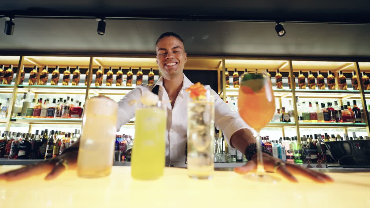 Barman sorridente che presenta quattro cocktail colorati in un bar moderno