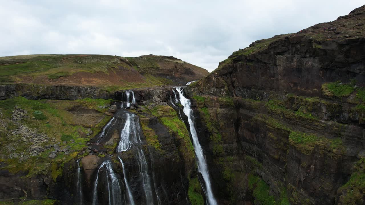 cortinas de agua sobre rocas volcánicas cubiertas de musgo verde en las cascadas de glymur, dolly aérea