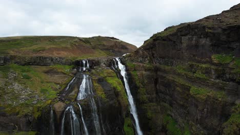 Cortinas-De-Agua-Sobre-Rocas-Volcánicas-Cubiertas-De-Musgo-Verde-En-Cascadas-De-Glymur,-Plataforma-Rodante-Aérea