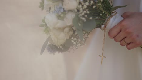 bride holding white bouquet with golden cross pendant and wedding ring visible