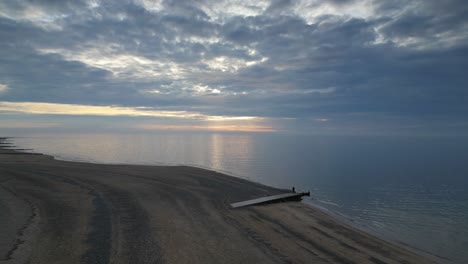 lone figure on jetty with reveal of coastline at sunset on fleetwood beach lancashire uk