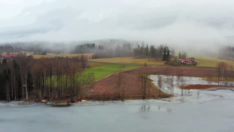 orbit shot of a farm next to a lake covered in fog in sweden