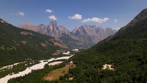 Idyllic-mountain-panorama-with-dense-forest-and-high-peaks-of-Alps-over-riverbed