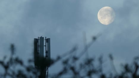 cloud passing moon behind cellular telecommunication transmitter tower