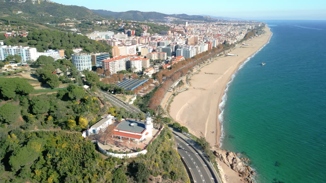 Luftfoto med drone af Calella de Mar på Maresme-kysten, Spanien, flyvning over hovedstranden og fyrtårnet.