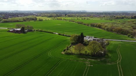 Vista-Aérea-De-Una-Casa-Rural-Inglesa-Rodeada-De-Exuberantes-árboles-Verdes-Y-Campos-Agrícolas