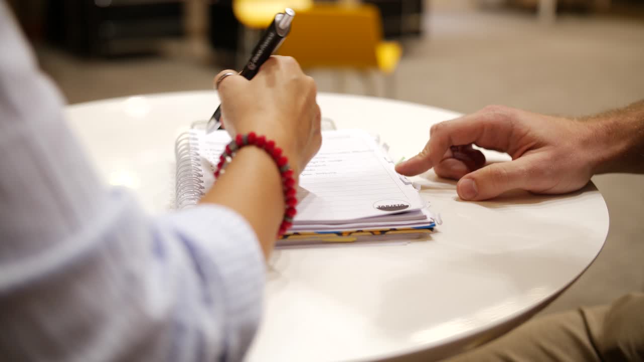 Close-up of Hands Writing Notes in a Notebook on a Table