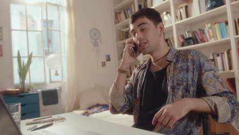 young man sitting with laptop at home and chatting on phone