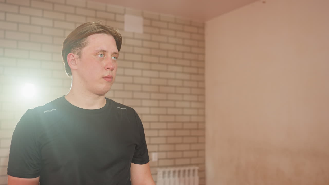 Wrestler with flushed face and focused expression stands in training gym wearing black sports shirt, concentration and determination visible, representing strength, preparation, in combat sports practice