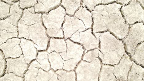 A-top-down-shot-zooms-out-from-broken-soil-due-to-drought,-highlighting-the-dry-grasses-and-climate-change-concept