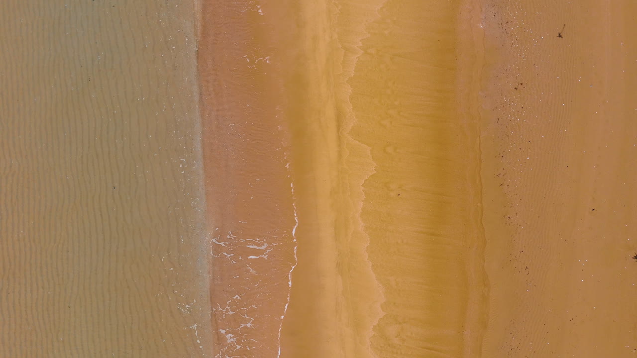 Top down view of empty wide sandy beach. Minimalist aerial shot of golden sand textures with slight water ripples on the left side