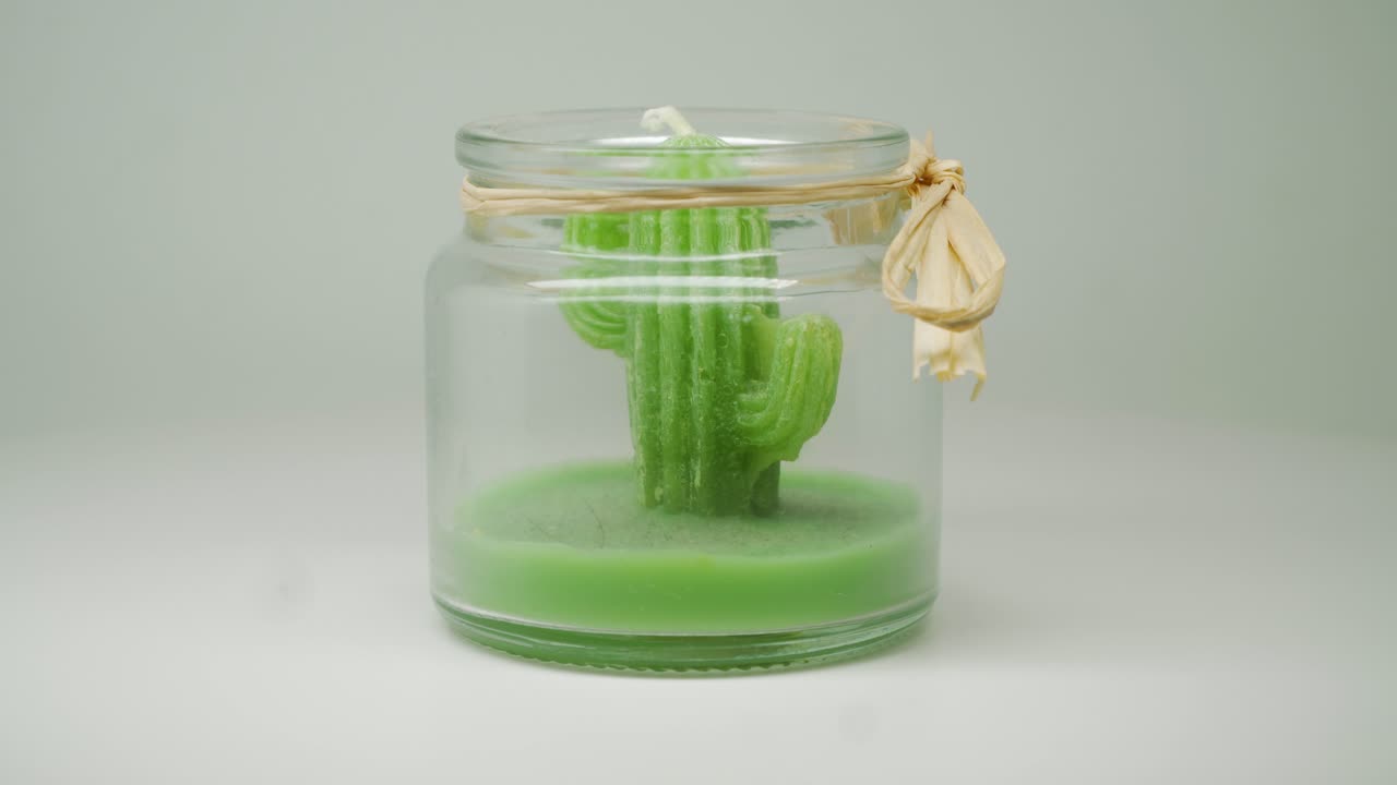 una vela de cera de cactus verde dentro de un frasco transparente moviéndose lentamente en un movimiento circular - primer plano
