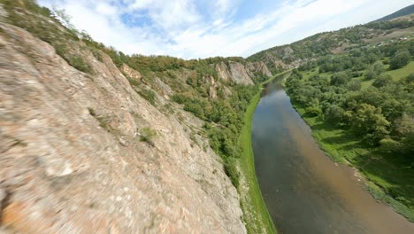 a shallow river flows near the sole of the mountain. light clouds move across the blue sky. the glare of the sun's rays is reflected on the surface of the water.