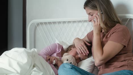 mother calling a doctor while her daughter lying ill in bed