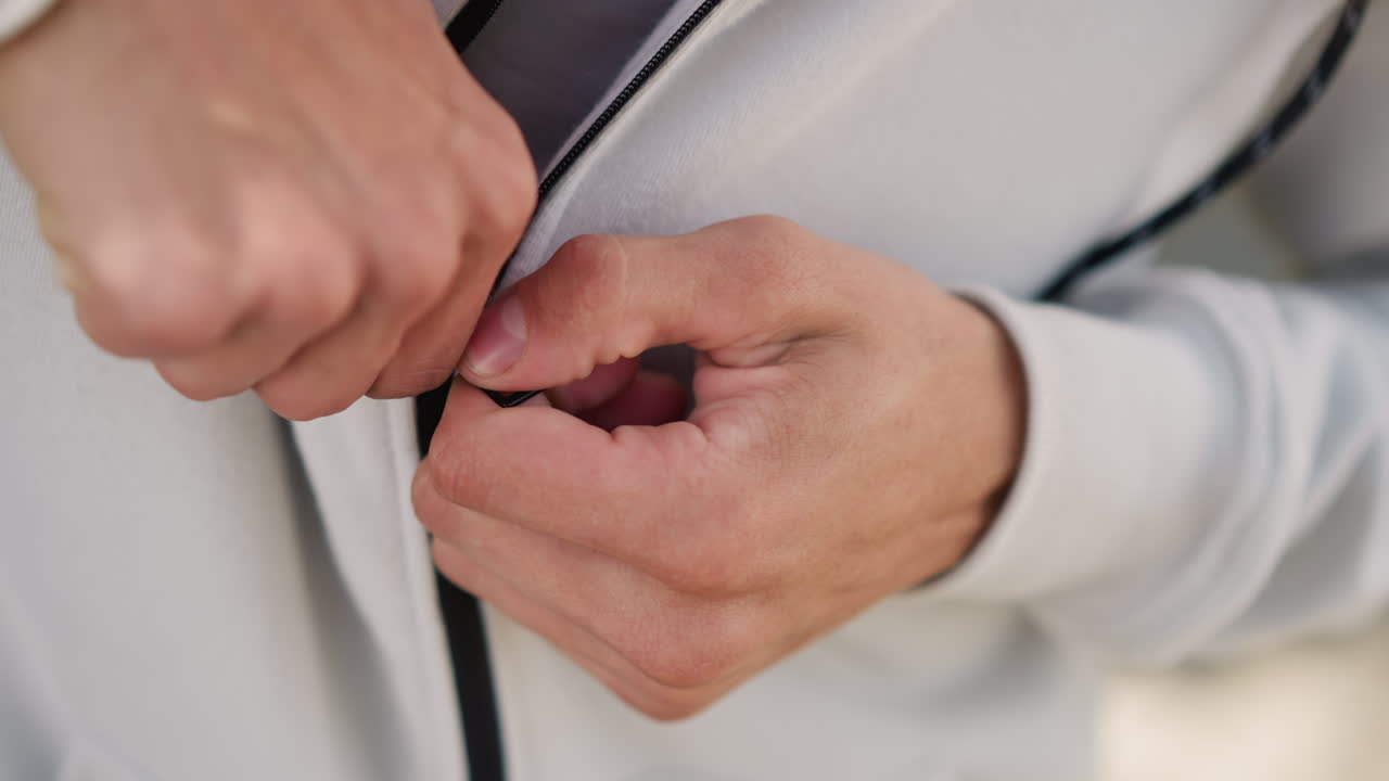 Male athlete securing hoodie for workout, Closeup of fingers tightening hoodie before running session, Active male sporting textured sportswear while adjusting hoodie under cloudy sky