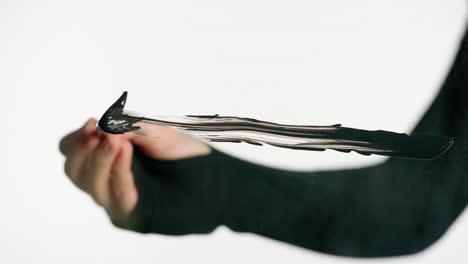 close-up of a hand painting a black stroke with a brush on a white background